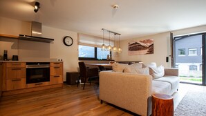 A modern kitchen with wooden cabinets, a built-in oven, and a dining area with a table and chairs. - 1102 Kristall 2 (Gaschurn)