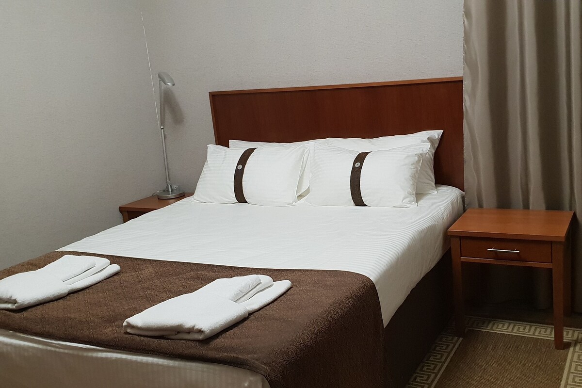 A neatly made bed with white and brown bedding, a wooden headboard, and a bedside table with a lamp.