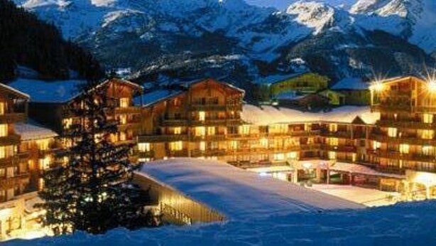 A multi-story lodge with a snow-covered ground, surrounded by mountains. - Studio for 3 in Valfréjus center, balcony and ski locker (Valfréjus)
