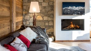 Ett mysigt vardagsrum med en vägg av natursten, en öppen spis, en väggmonterad TV och en bekväm soffa med dekorativa kuddar.