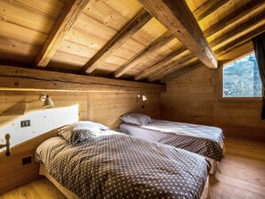 Une cabane avec deux lits, des murs en bois, un plafond en pente et une fenêtre donnant sur un paysage enneigé.