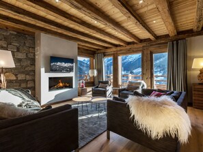 Un salon chaleureux avec une cheminée, des sièges confortables et de grandes fenêtres offrant une vue sur les montagnes.
