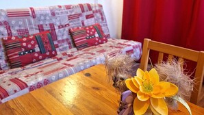 Une pièce chaleureuse avec une table en bois, un canapé agrémenté de coussins à motifs et un vase contenant une fleur jaune.