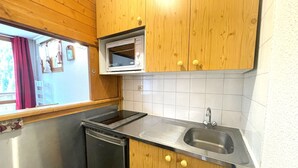 Une cuisine compacte avec des meubles en bois, un four à micro-ondes encastré, un évier en acier inoxydable et un lave-vaisselle.
