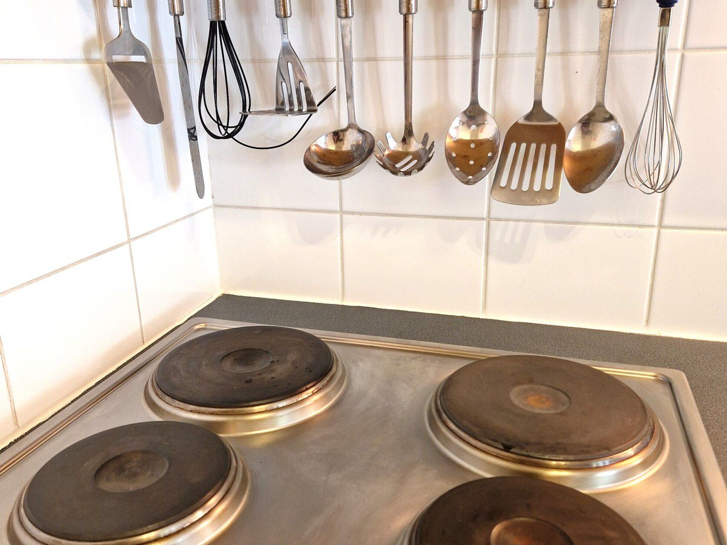 A kitchen with four stainless steel stovetops and various hanging utensils.