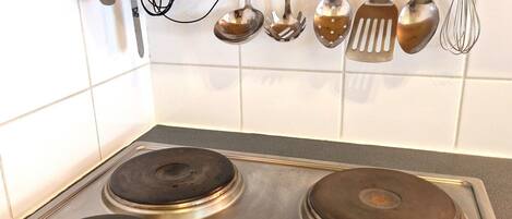 A kitchen with four stainless steel stovetops and various hanging utensils.