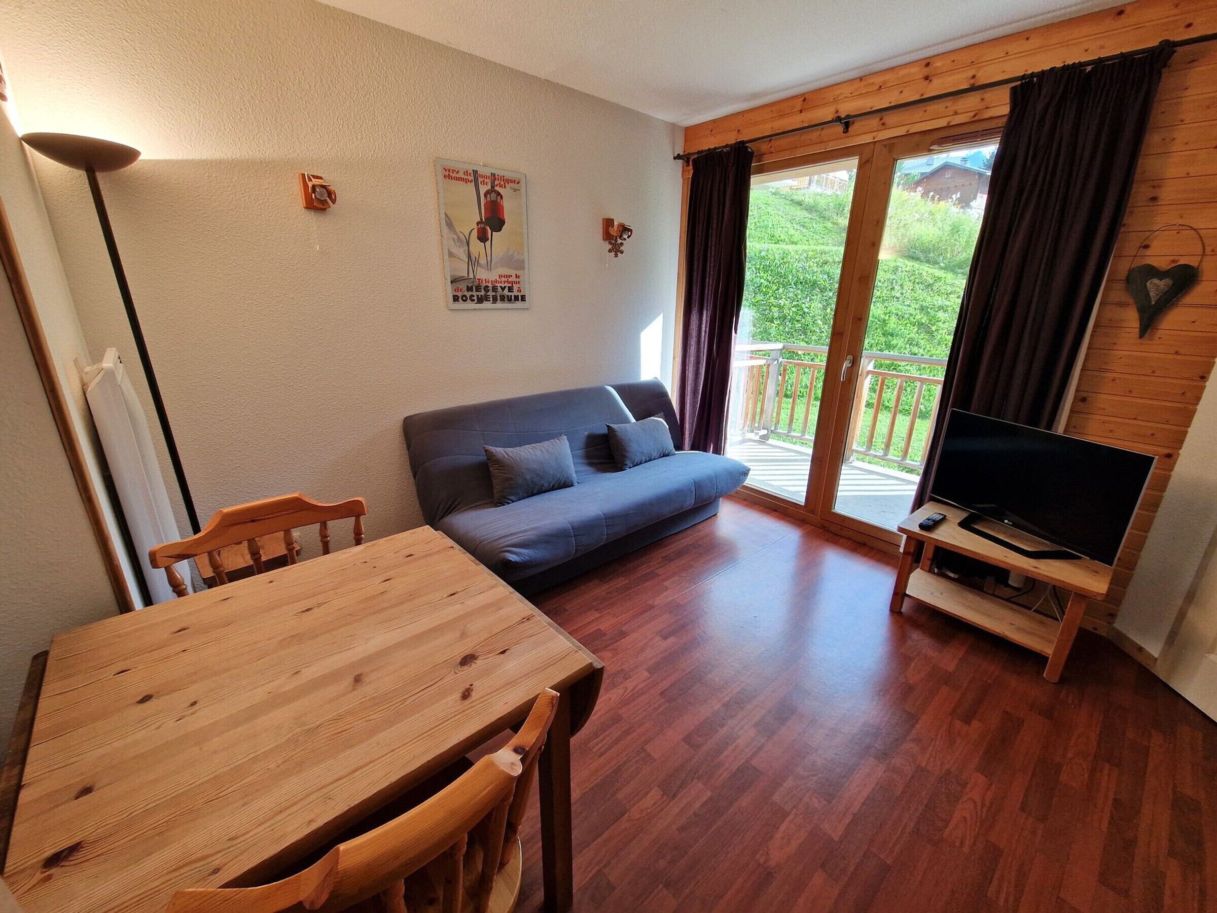 Una sala de estar acogedora con una mesa de madera, un sofá y un televisor sobre un mueble de madera.