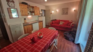 Un espace de vie compact comprenant un coin repas, une kitchenette et un canapé rouge.