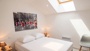Een slaapkamer met een bed, nachtkastje, lamp, stoel, radiator en dakraam.
