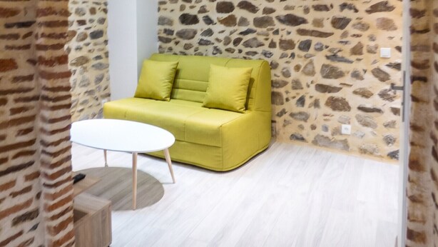 Een kamer met een stenen muur, een groene bank, een ronde witte tafel en een houten vloer.