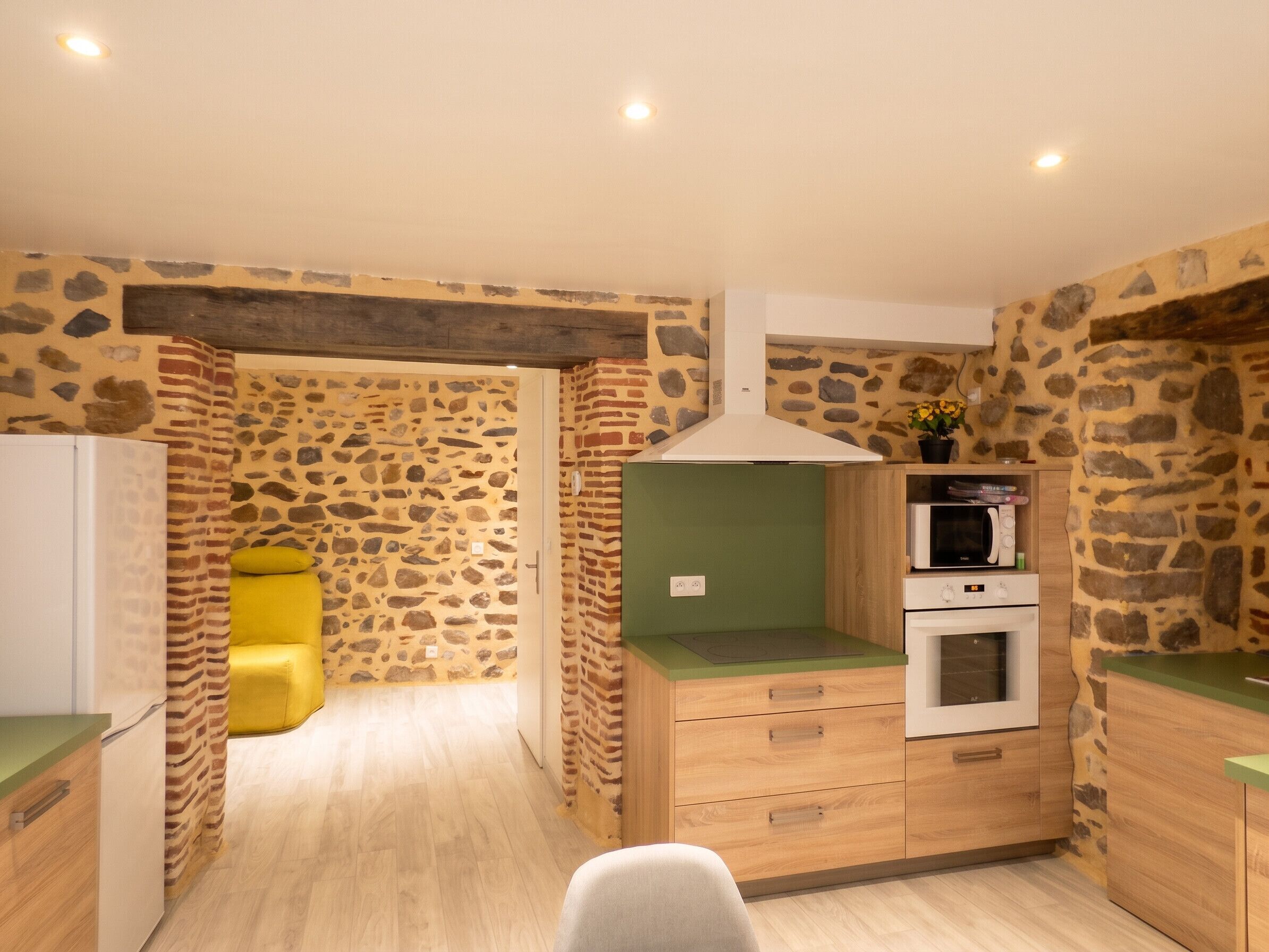 Une cuisine compacte avec un mur en pierre, un four à micro-ondes, un four traditionnel et un plan de travail vert.
