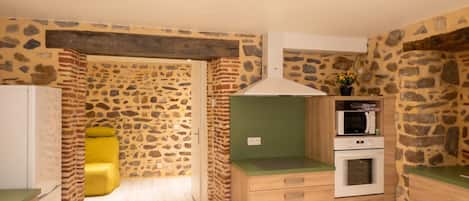 Cocina compacta con diseño de pared de piedra, microondas, horno y encimera verde.