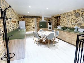 A dining area with a stone wall, a wooden table, and chairs. - Homerez - House in Brioude (Brioude)