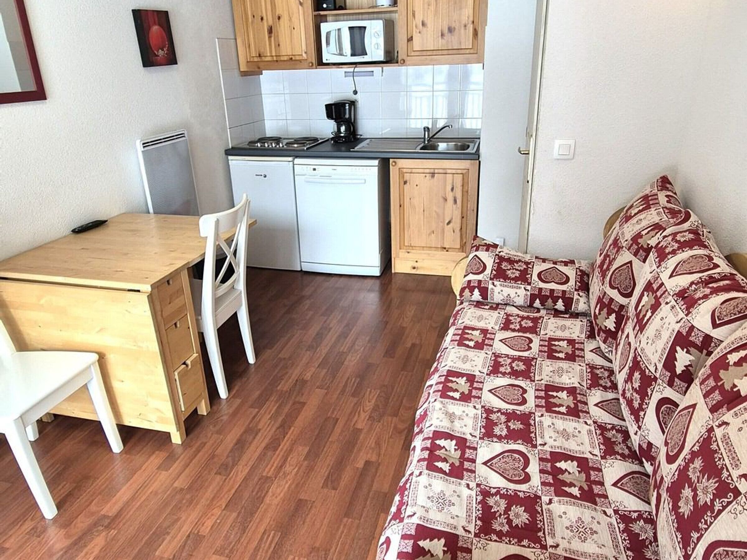 Eine kleine Küche mit Mikrowelle, Herd und Spüle. Ein Holztisch mit einem Stuhl und ein gemustertes Sofa sind ebenfalls vorhanden.