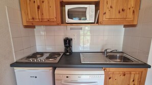 A compact kitchen with wooden cabinets, a microwave, a coffee maker, a dishwasher, and a sink.