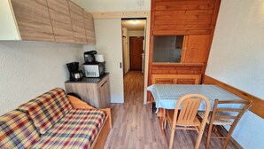 A compact living space with a sofa, a small table with chairs, a kitchenette, and a wooden cabinet. - Studio for 4 in Valfréjus center with balcony, equipped kitchen, ski locker (Valfréjus)