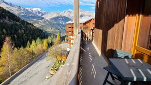 A balcony with a view of a mountain range, a wooden building, and a table with a bench. - Studio for 4 in Valfréjus center with balcony, equipped kitchen, ski locker (Valfréjus)