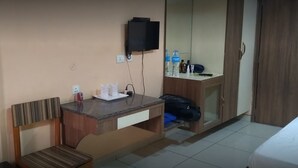 Habitación de hotel con cama, escritorio y silla, televisor montado en la pared y armario.
