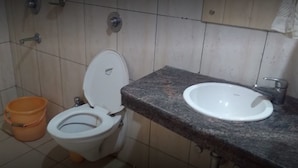 Un baño con inodoro, lavamanos y un balde.