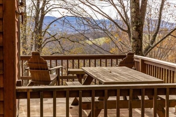 Una terraza de madera con una mesa y sillas, con vistas a un paisaje montañoso.