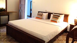 Ein Hotelzimmer mit einem großen Bett, einem hölzernen Kopfteil, einem Nachttisch und einem Beistelltisch. Eine Tür führt in einen anderen Raum, und ein Wandbild ist angebracht.