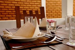 A dining table set with plates, cutlery, and glasses, with a brick wall in the background. - Naturehawks Safari Villa Yala (Thissamaharama)