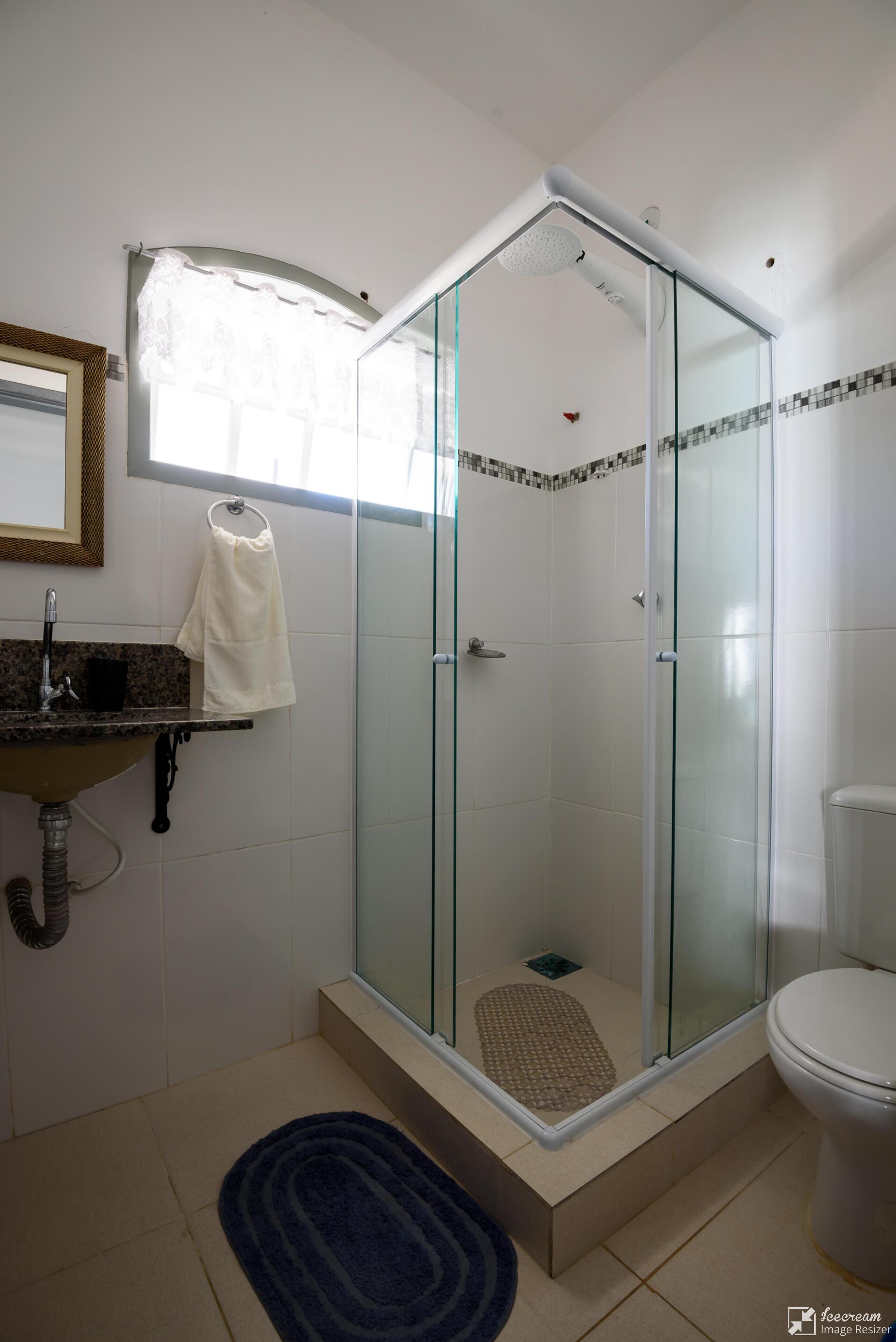 Un bany amb dutxa tancada amb vidre, un lavabo amb penjador de tovalloles i un vàter.