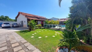 A residential property with a well-maintained lawn, a swimming pool, and a garage with two cars parked. - Village Itaúna Inn – Beach Houses (Saquarema)