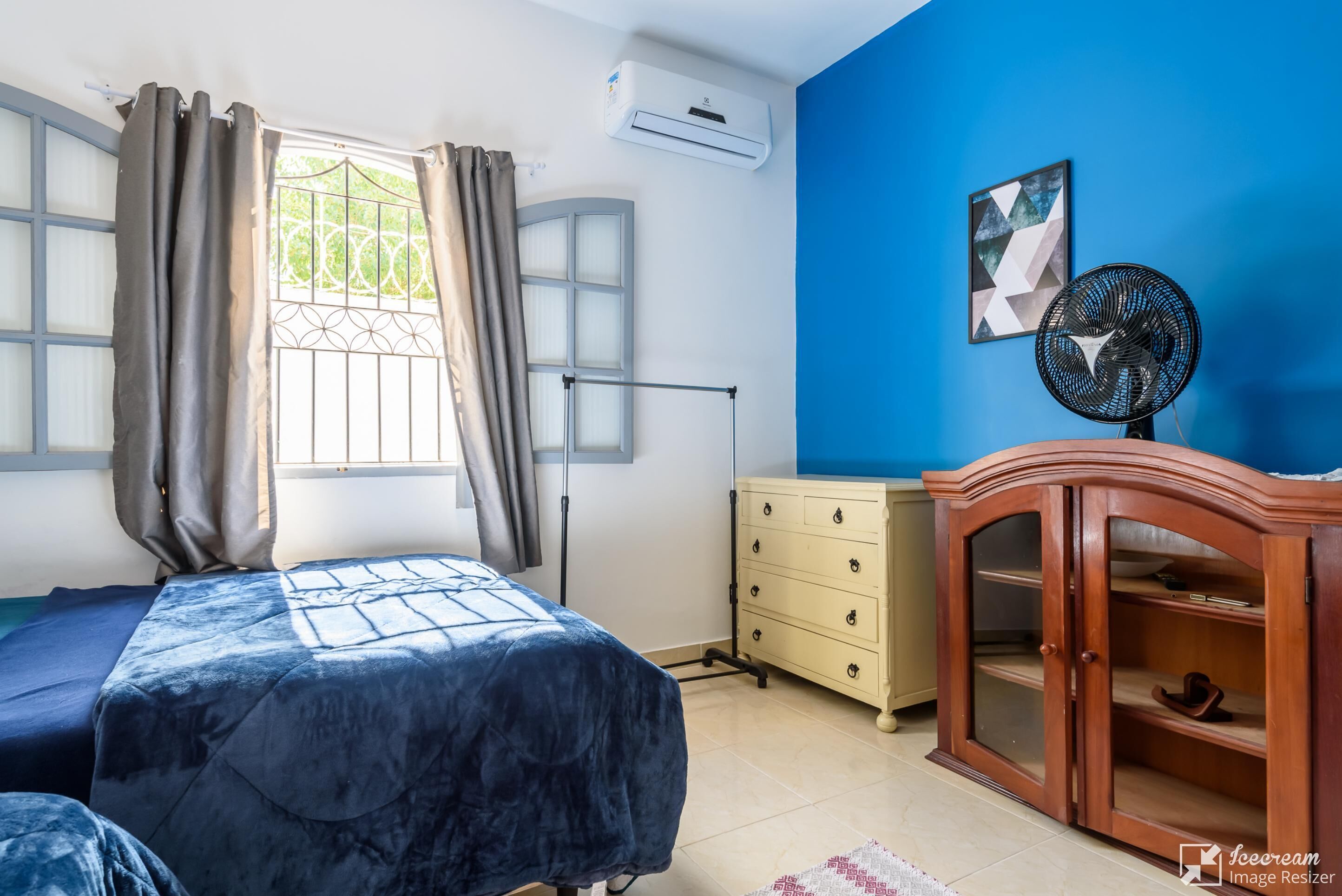 Un dormitorio con cama, cómoda, ventilador y ventana con cortinas.