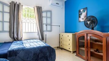 Un dormitorio con cama, cómoda, ventilador y ventana con cortinas.