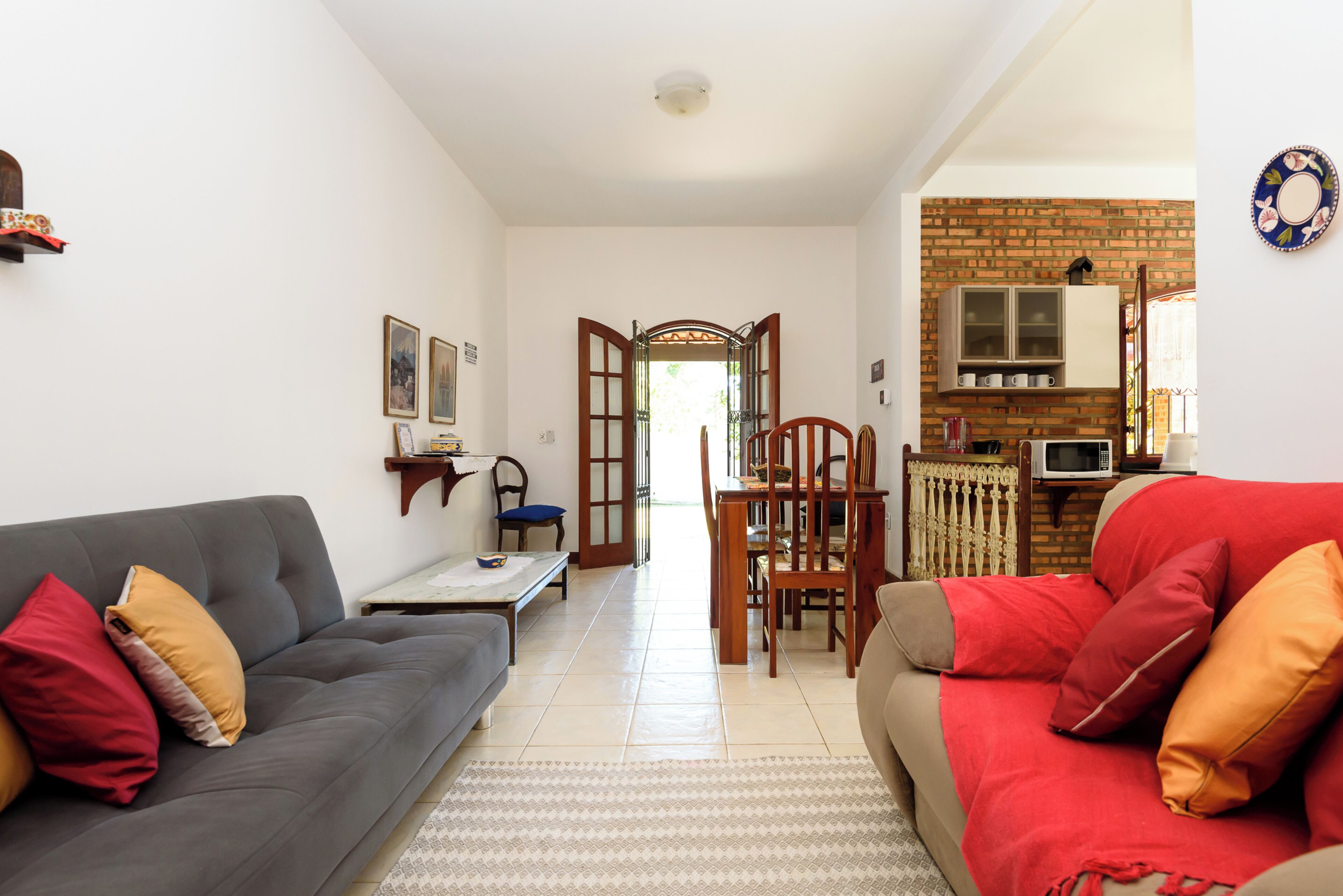 Una sala de estar con un sofá gris, un sofá rojo y una mesa de comedor con sillas. Hay una zona de cocina con microondas y armarios.