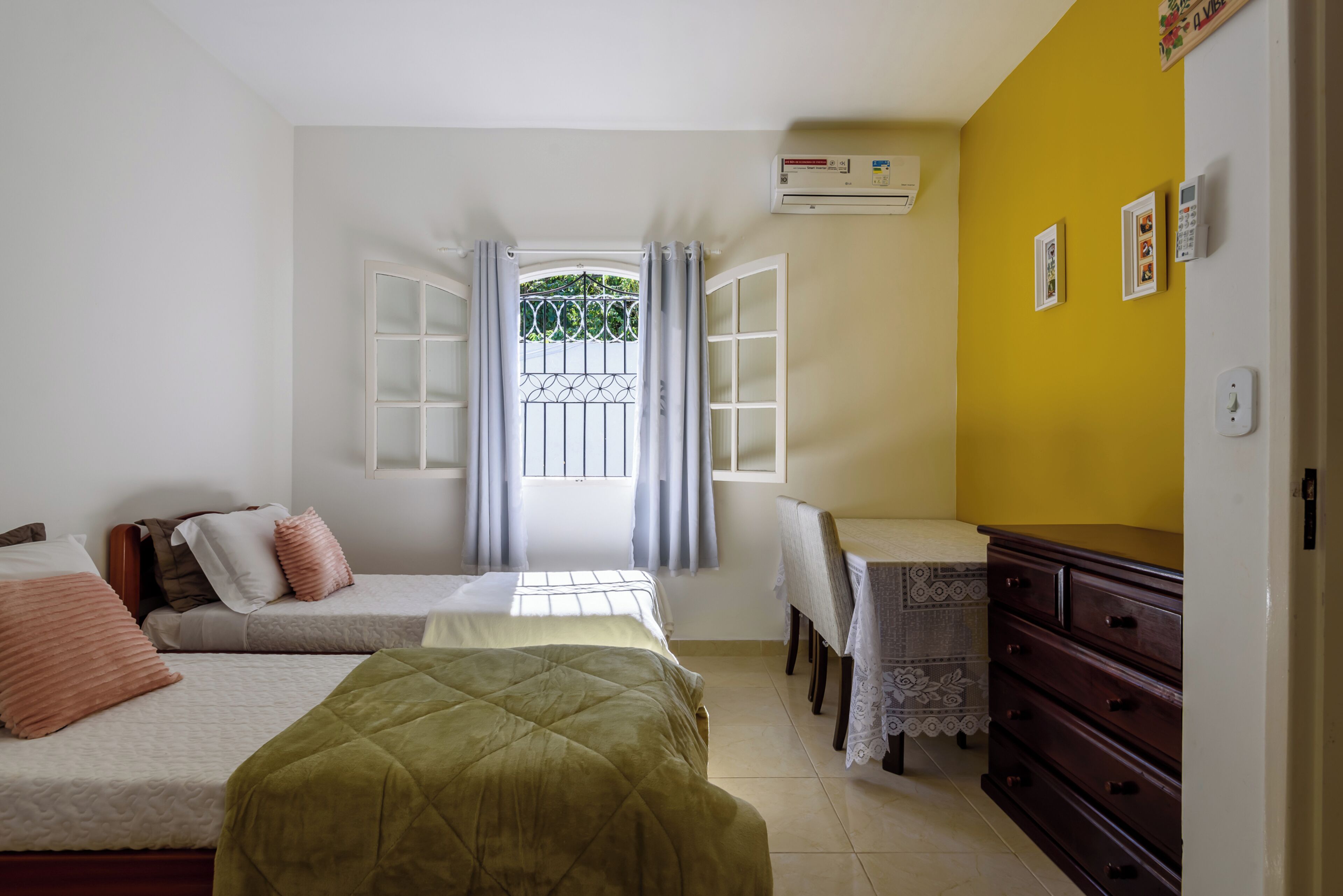 A bedroom with two beds, a desk, a dresser, and a window with curtains.