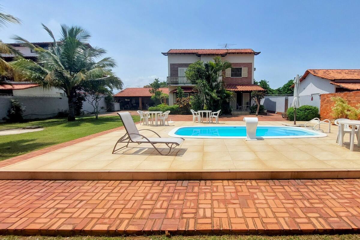 Un patio trasero con piscina, sillas de descanso y zona de comedor.