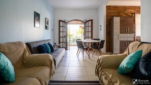 A living room with two sofas, a dining table with chairs, and a kitchen area with cabinets. - Village Itaúna Inn – Beach Houses (Saquarema)