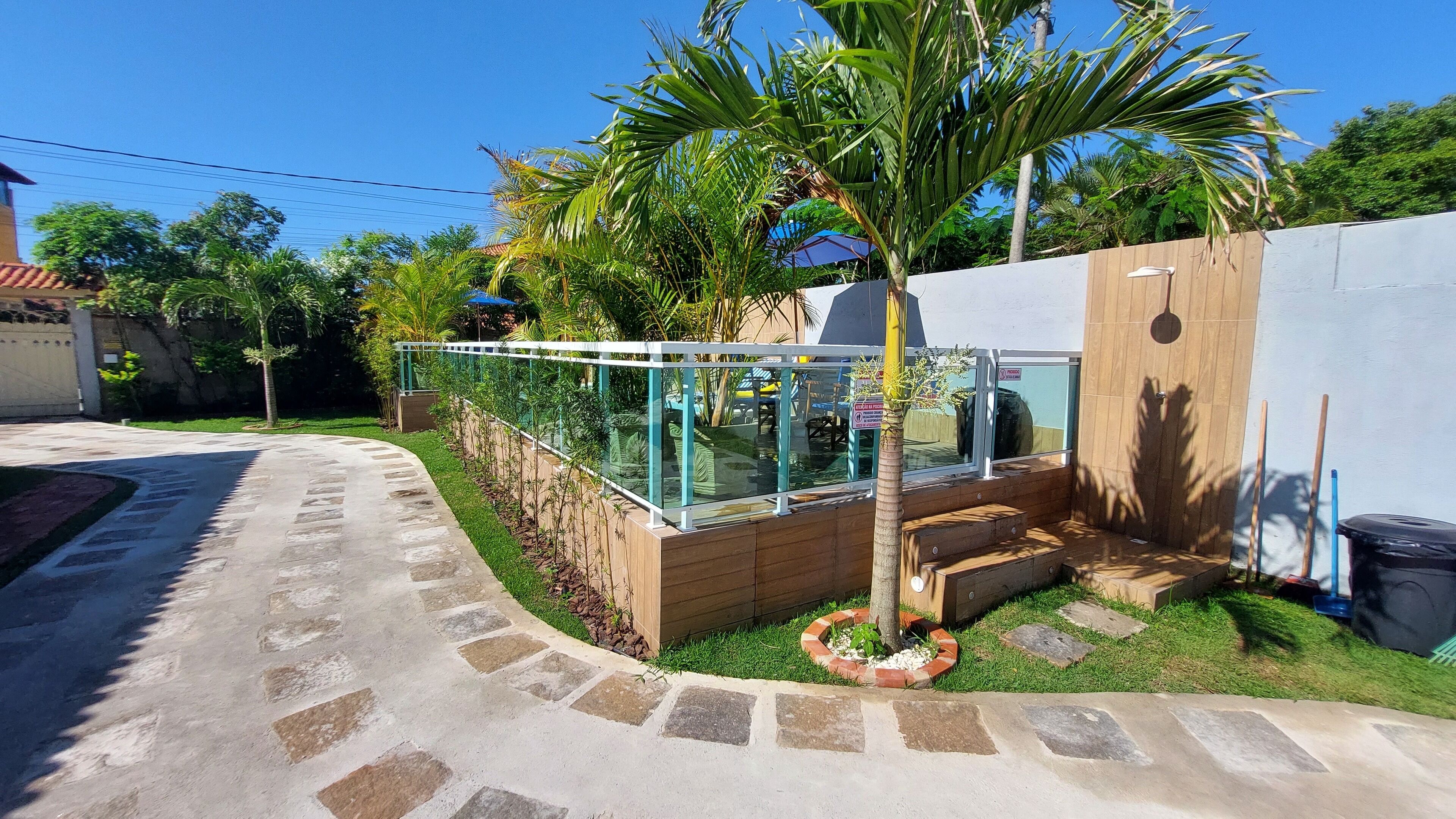 Un espacio exterior moderno con cerramiento de vidrio, escalones de madera y una palmera.