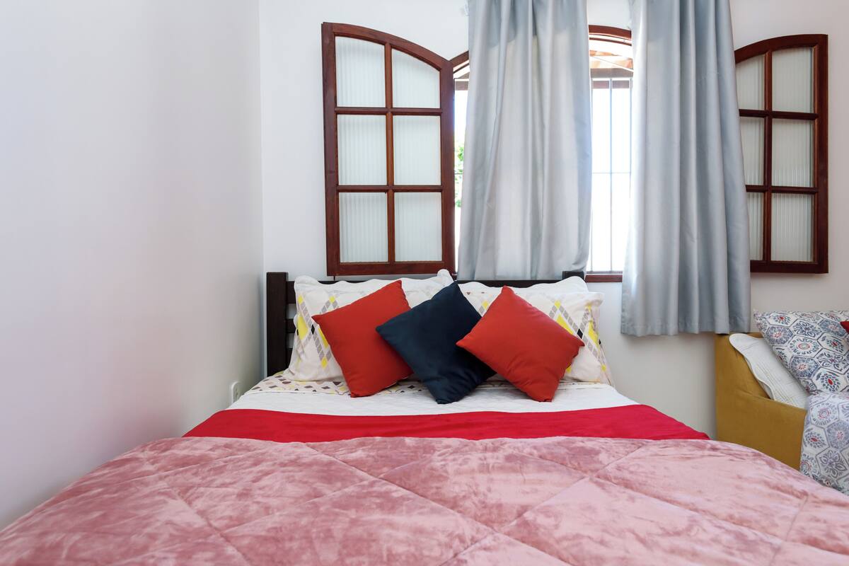 Una cama con un edredón rojo y rosa, dos almohadas rojas y una almohada azul.