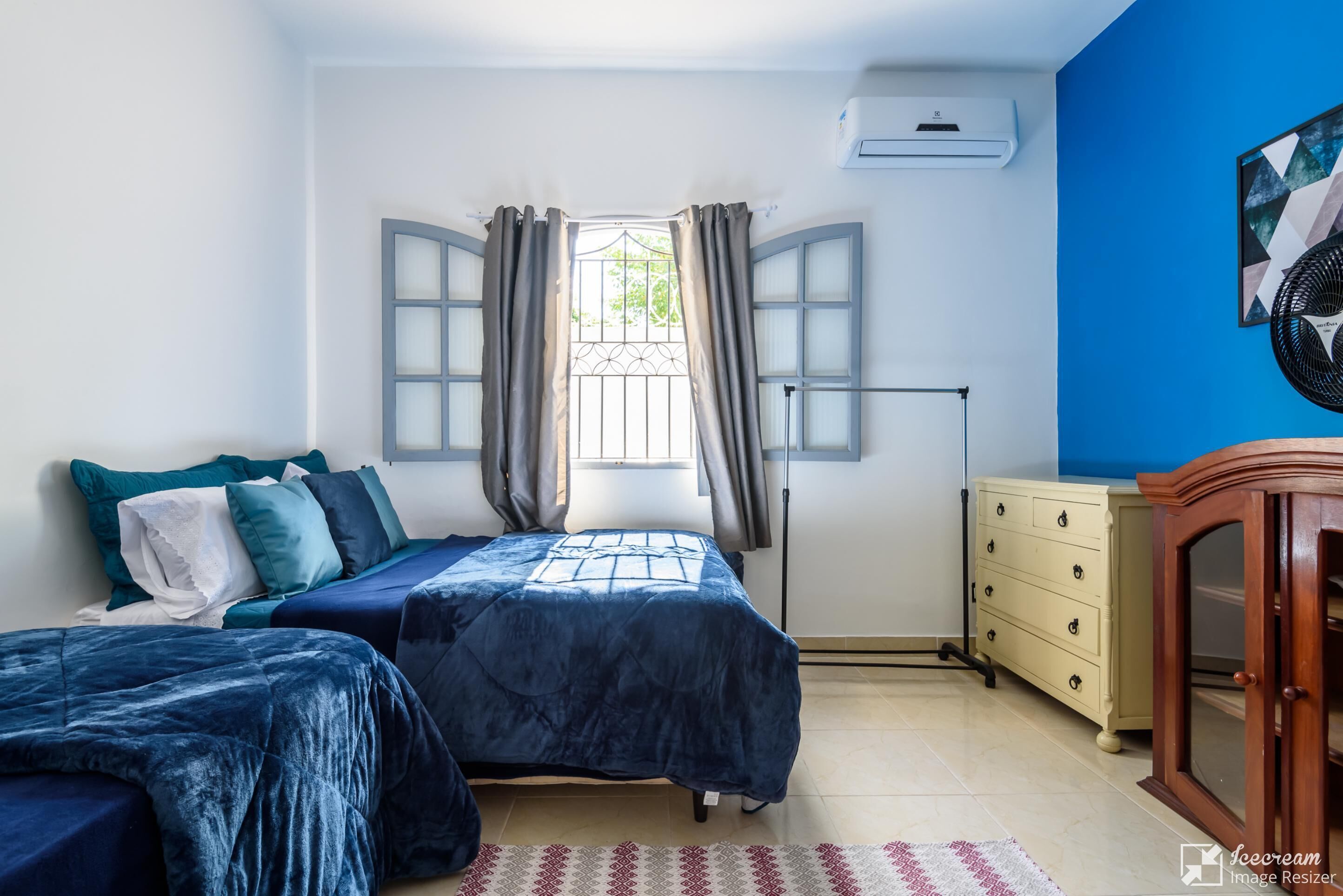 A bedroom with two beds, a dresser, and a window with curtains.