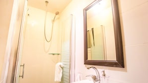 Een badkamer met een douche, wastafel en spiegel.