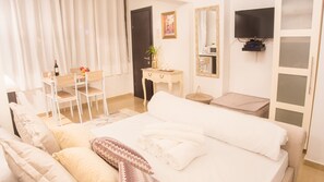 Quarto de hotel com cama, escrivaninha, cadeira, televisão e janela com cortinas.
