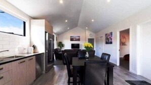 A modern kitchen with a dining area, wooden flooring, and a large window. - NV Homes (Lake Hayes)