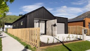 A modern two-story house with a black exterior, a wooden fence, and a driveway. - NV Homes (Lake Hayes)