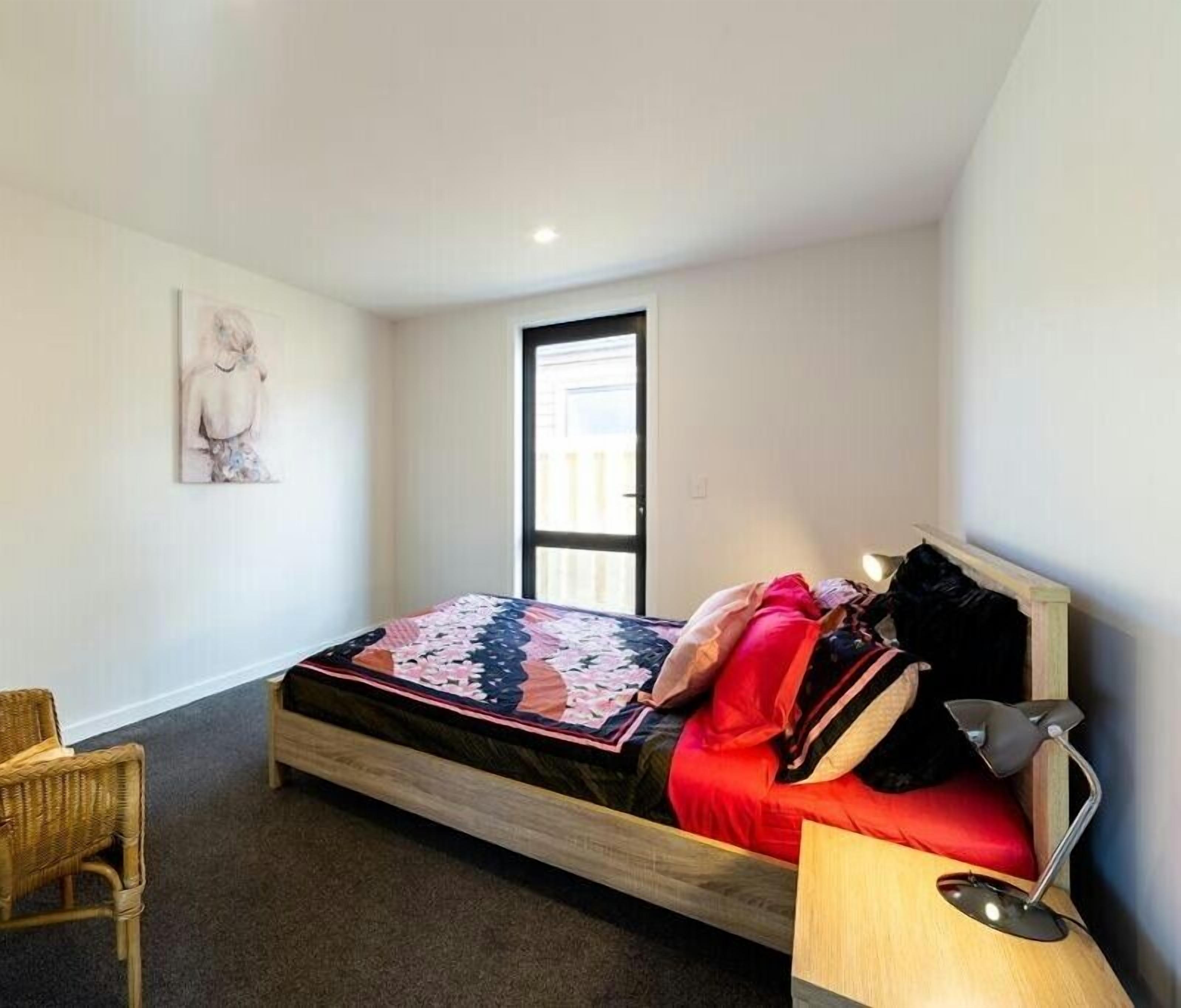 Une chambre à coucher avec un lit, une chaise, un bureau, une lampe et une porte.