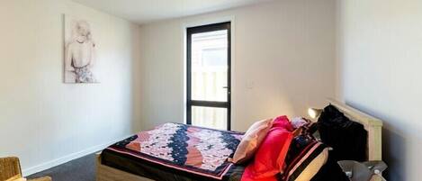 Une chambre à coucher avec un lit, une chaise, un bureau, une lampe et une porte.