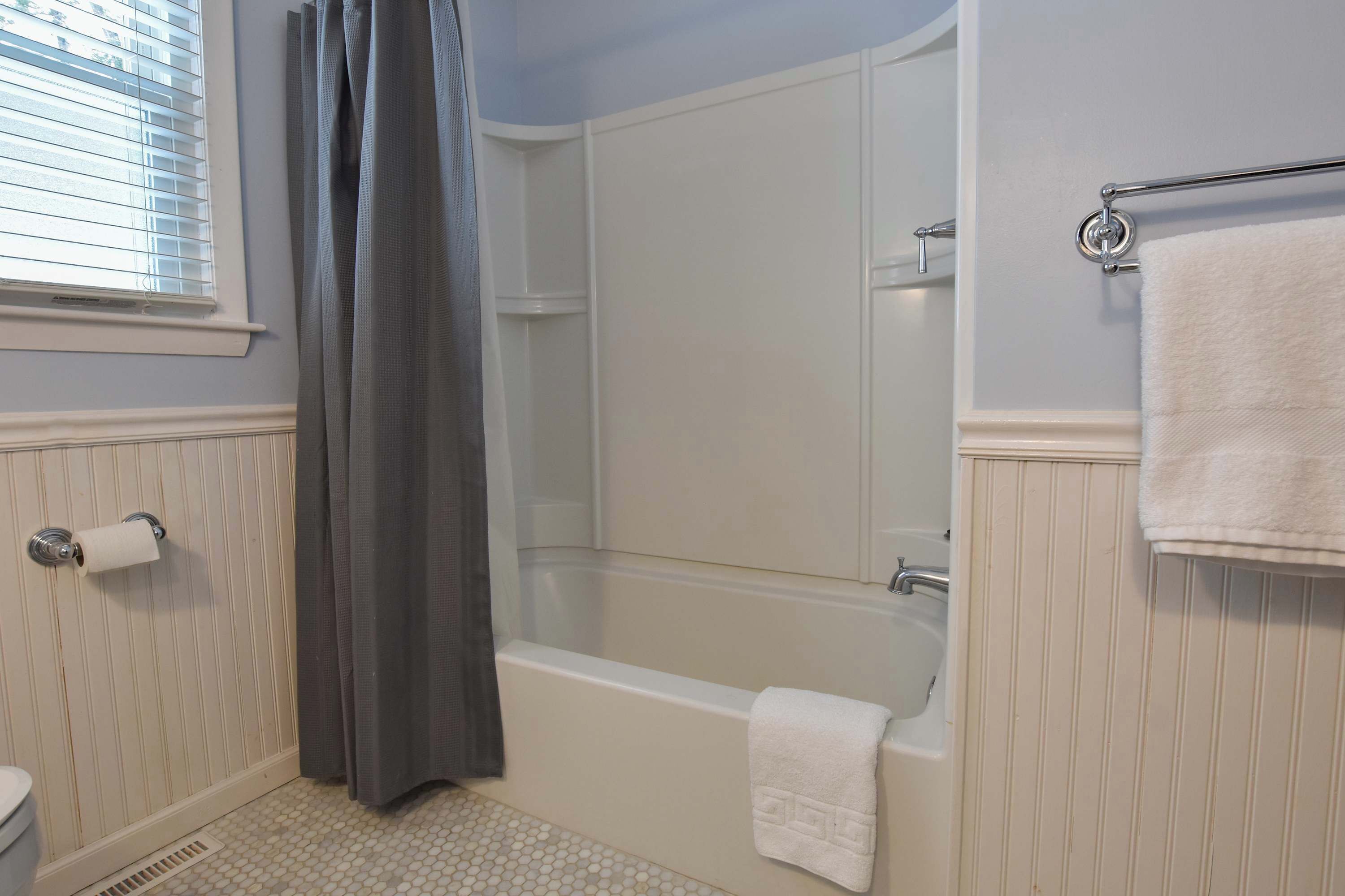 Un baño con bañera, ducha, inodoro y ventana con persianas.