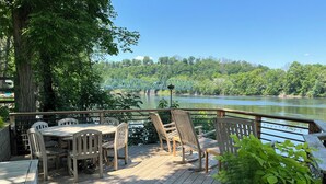 Eine Holzterrasse mit Tisch und Stühlen mit Blick auf einen Fluss, im Hintergrund eine Brücke.