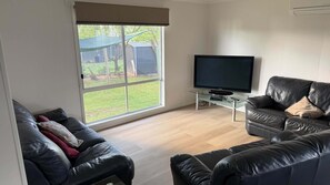 Een woonkamer met een groot raam, een flatscreen televisie en twee leren banken.
