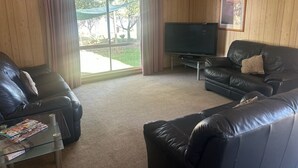 Una sala de estar con dos sofás de cuero negro, una mesa de centro de vidrio, un televisor de pantalla plana y un ventilador de techo.