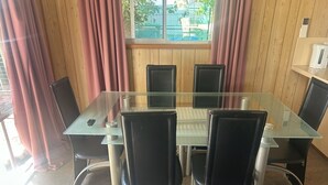 Un salón de conferencias con una mesa de vidrio y sillas negras, paneles de madera y un ventanal con cortinas.