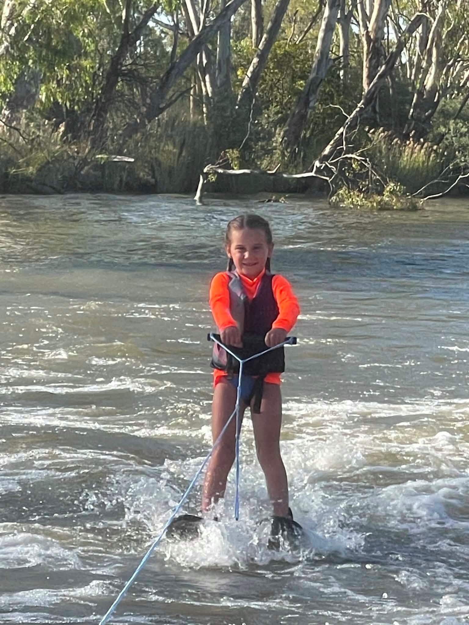 A person water skiing on a river with trees in the background.