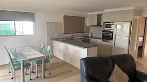 Una cucina moderna con un'isola centrale, un'area pranzo con un tavolo in vetro e sedie, e un divano in pelle nera.
